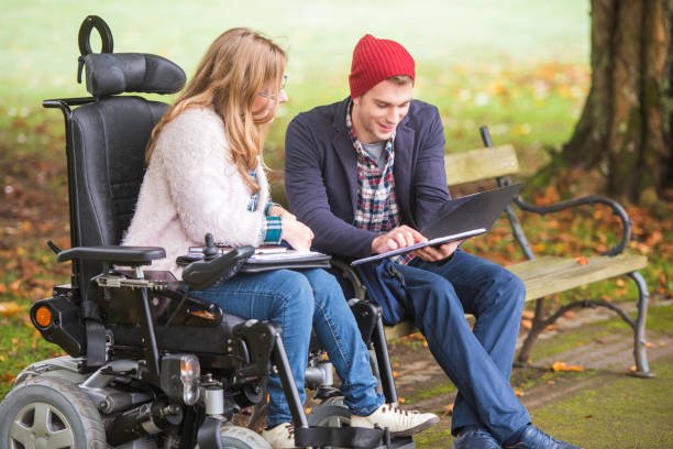 Two friends, one on a wheelchair, studying together at the park.